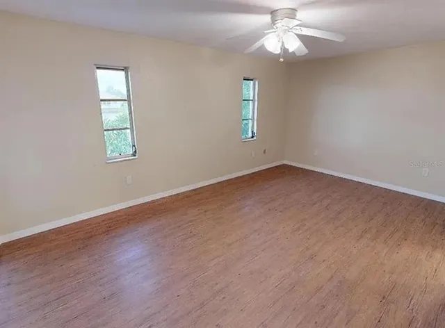 an empty room with wooden floor chandelier fan and windows