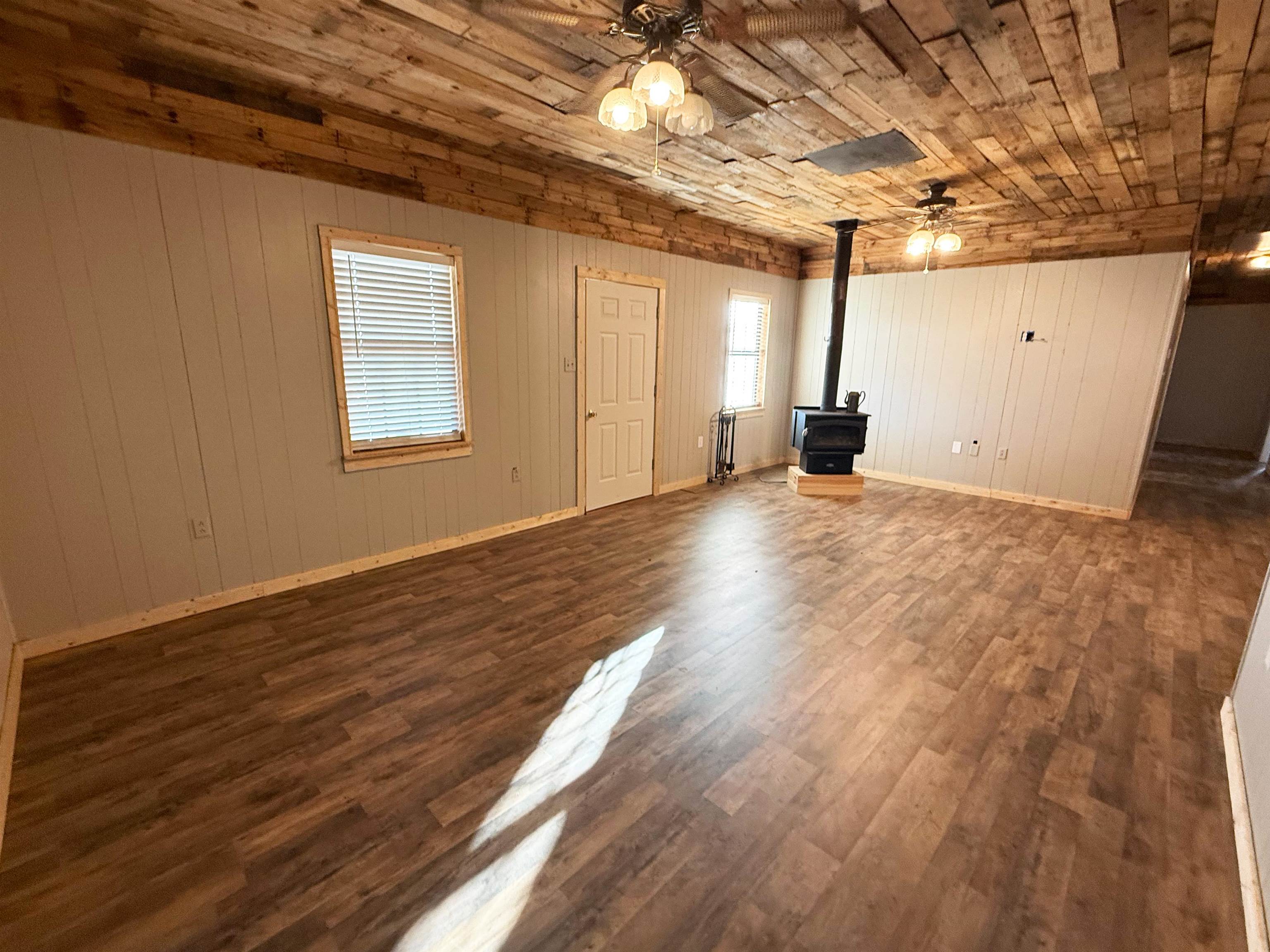 2142 Highway 70 Mason, TN 38049 - Photo 9 of 36 Unfurnished living room with a ceiling fan, a wood stove, dark wood-style flooring, wood walls, and wooden ceiling