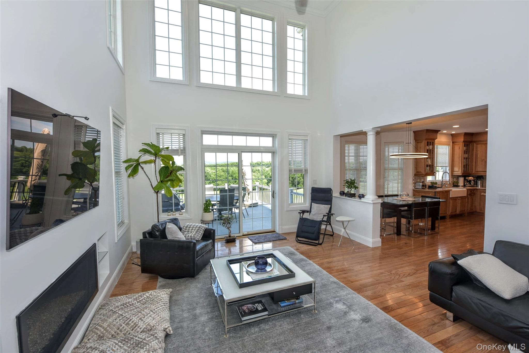 46 Mansion Ridge Boulevard Monroe, NY 10950 - Photo 22 of 46 Vaulted living area with wood-finish flooring, featuring a linear fireplace, multiple large windows, and sliding glass doors opening to an outdoor deck