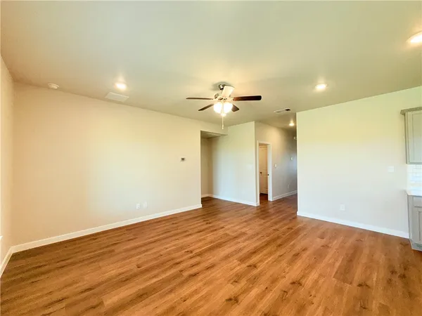 a view of an empty room with wooden floor and a ceiling fan