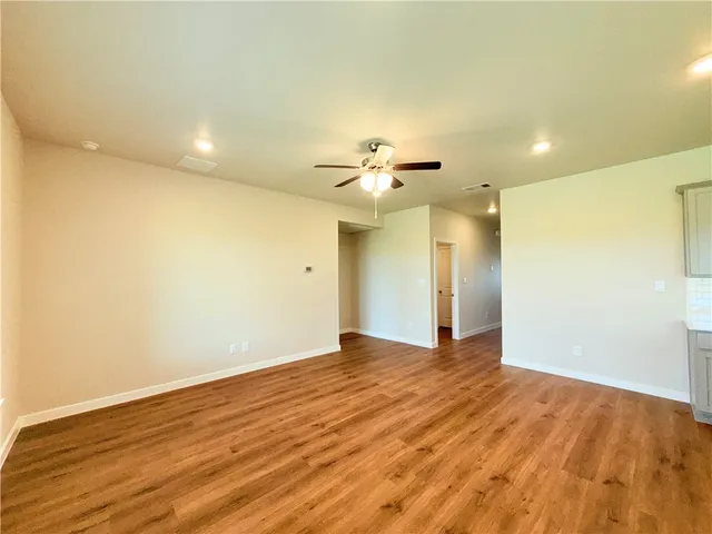 a view of an empty room with wooden floor and a ceiling fan