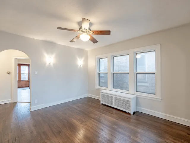 an empty room with wooden floor fan and windows