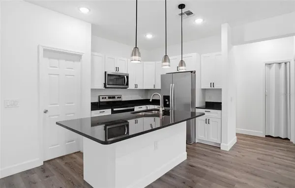 a kitchen with stainless steel appliances a stove a refrigerator a sink and white cabinets with wooden floor
