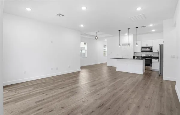 an empty room with wooden floor and kitchen view