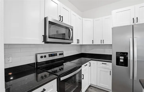 a kitchen with stainless steel appliances granite countertop white cabinets a stove a microwave and a refrigerator