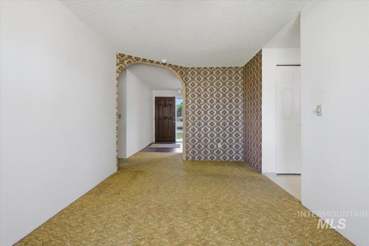 1311 North Middleton Road Nampa, ID 83651 - Photo 34 of 49 Entryway featuring a dark wood front door, patterned wallpaper accent, arched doorway, and textured ceiling