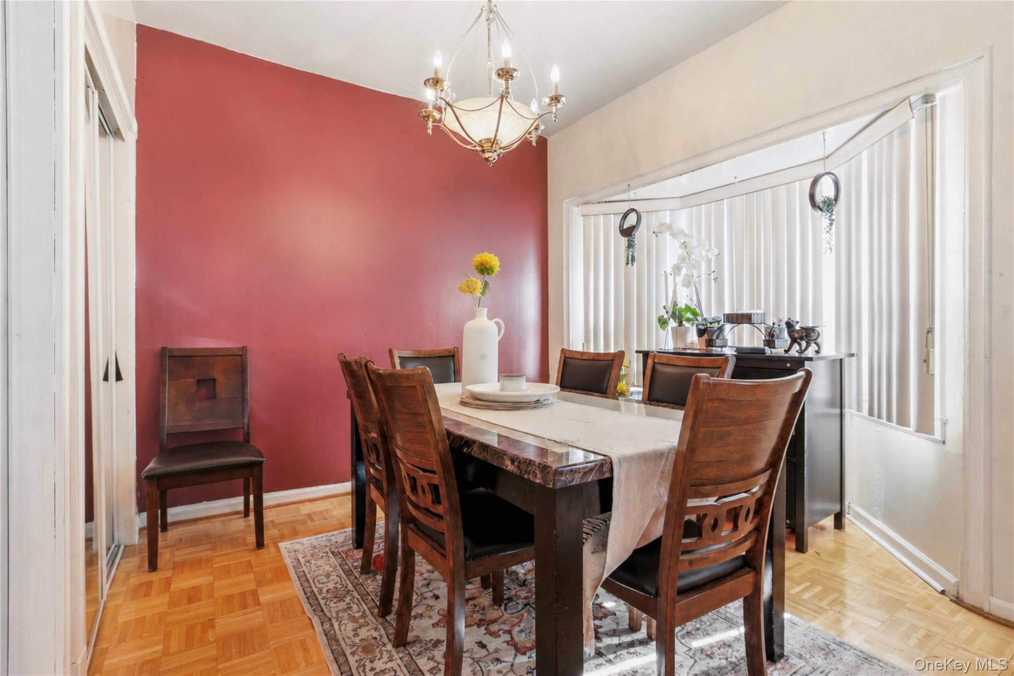 83-39 252nd Street Queens, NY 11426 - Photo 5 of 26 Dining area featuring a prominent red accent wall, parquet wood-finish flooring, and an elegant chandelier