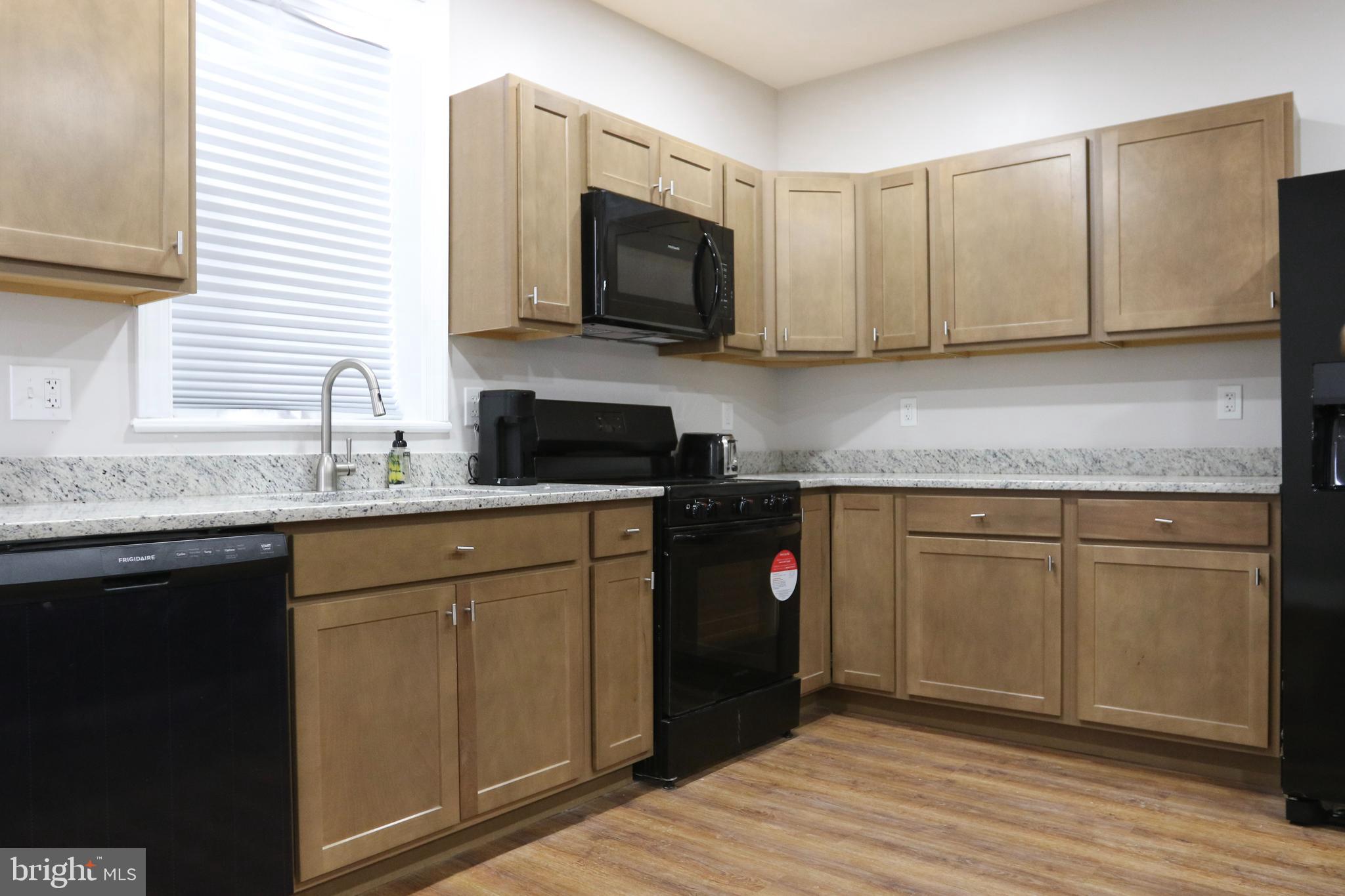 3908 Primrose Avenue Baltimore, MD 21215 - Photo 6 of 19 a kitchen with stainless steel appliances granite countertop a sink a stove a microwave and wooden cabinets
