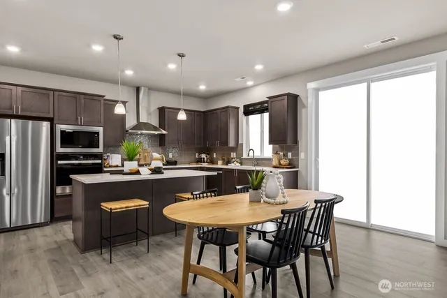 a kitchen with kitchen island granite countertop a dining table chairs refrigerator and microwave