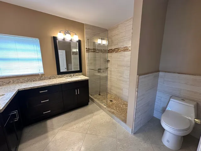 a bathroom with a granite countertop sink a toilet a mirror and shower