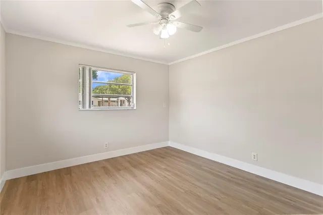 a view of an empty room with wooden floor and a ceiling fan