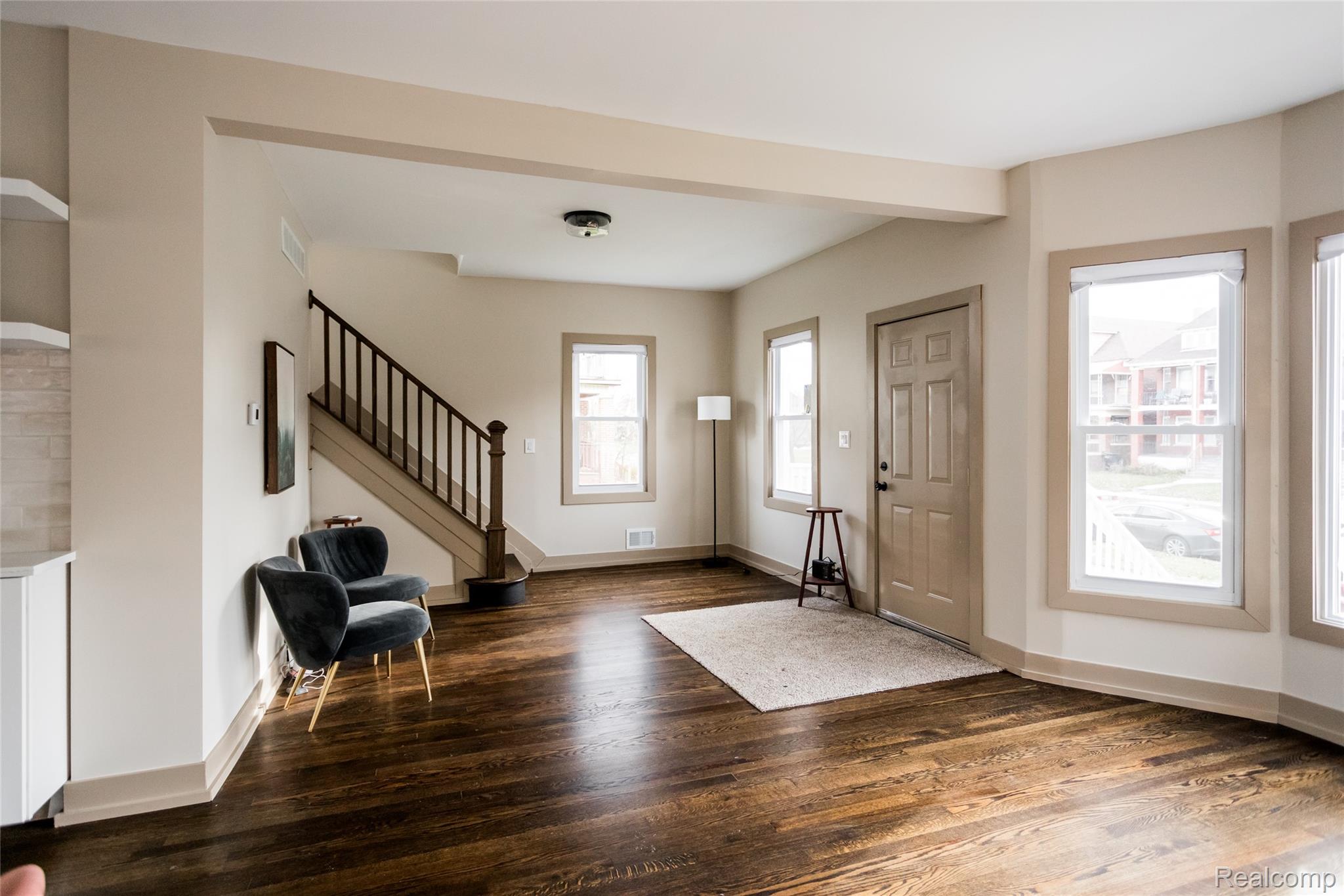 2630 Harding Street Detroit, MI 48214 - Photo 7 of 30 Expansive living area with rich, dark wood-finish flooring, abundant natural light from multiple windows, and a classic staircase featuring dark wood balusters and a contrasting handrail