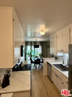a kitchen with a sink dishwasher a stove and white cabinets with wooden floor