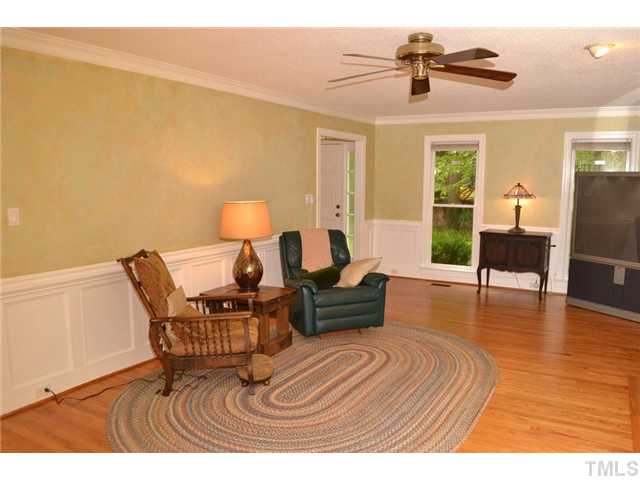 901 Streamer Court Raleigh, NC 27614 - Photo 6 of 21 Large living room with hardwood floor, raised paneling, crown molding, two large windows, and a ceiling fan