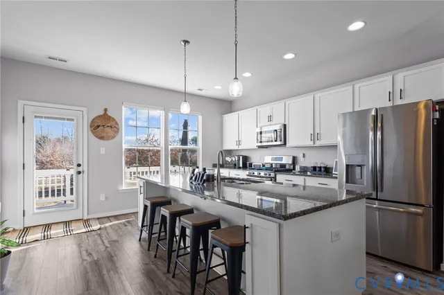 a kitchen with granite countertop a refrigerator a stove a dining table and chairs with wooden floor