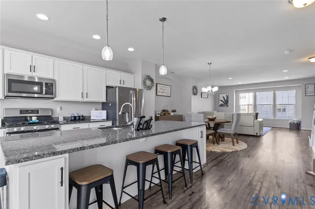 a kitchen with stainless steel appliances granite countertop a stove top oven a sink dishwasher a dining table and chairs with wooden floor