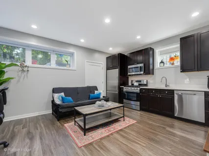 a living room with stainless steel appliances furniture a rug kitchen view and a window