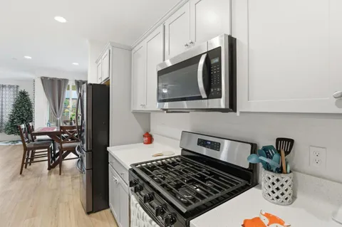 a kitchen with stainless steel appliances a stove a microwave a refrigerator white cabinets and wooden floor