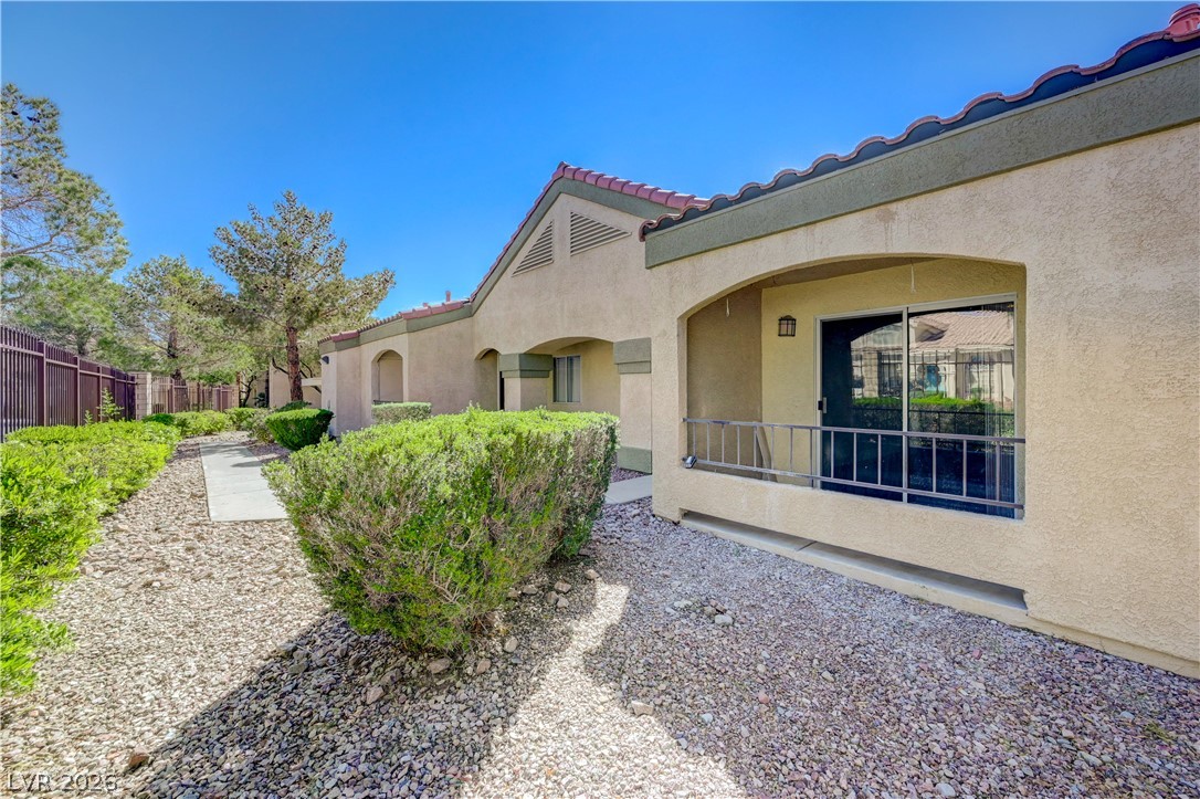 7885 West Flamingo Road, Unit 1050 Las Vegas, NV 89147 - Photo 3 of 62 A terracotta-tiled roofline crowns this stucco residence, nestled amidst mature desert landscaping.