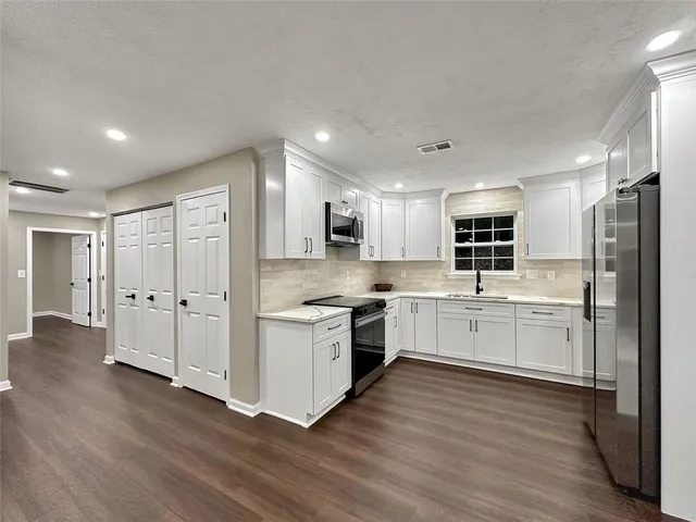 a large kitchen with stainless steel appliances granite countertop a stove top oven a sink dishwasher and a refrigerator with wooden floor