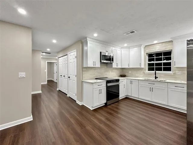 a kitchen with stainless steel appliances kitchen island granite countertop a stove a sink and white cabinets with wooden floor