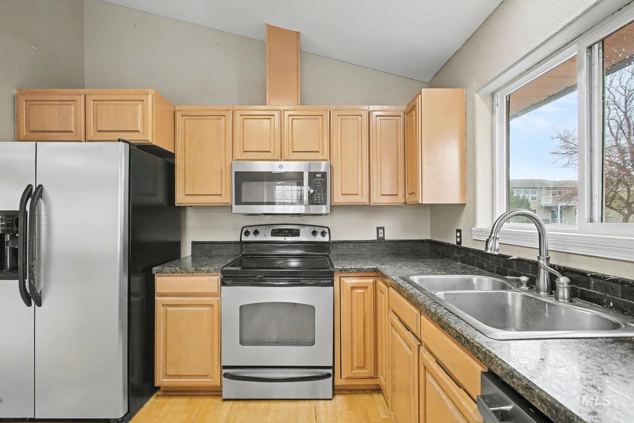 2242 Chukar Lane Clarkston, WA 99403 - Photo 16 of 41 Kitchen featuring stainless steel appliances, vaulted ceiling, dark countertops, light brown cabinetry, and light wood-type flooring