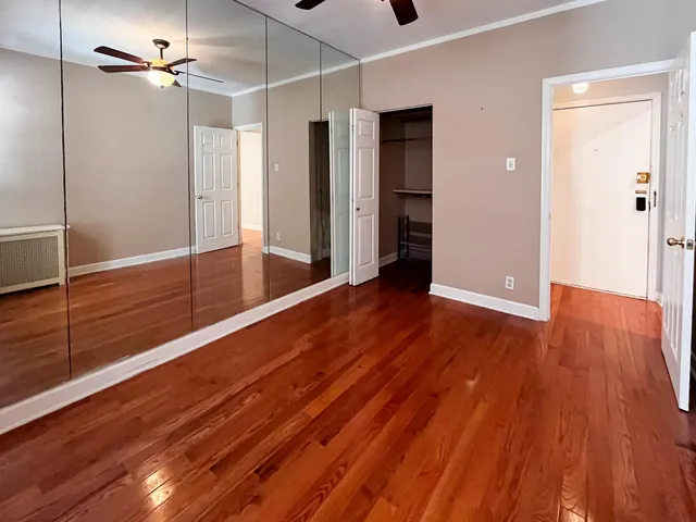 a view of an empty room with wooden floor and a ceiling fan