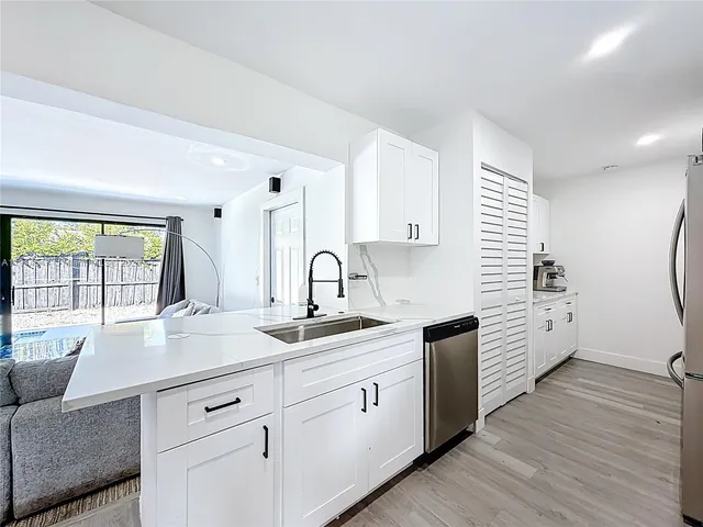 a kitchen with a sink dishwasher and white cabinets with wooden floor