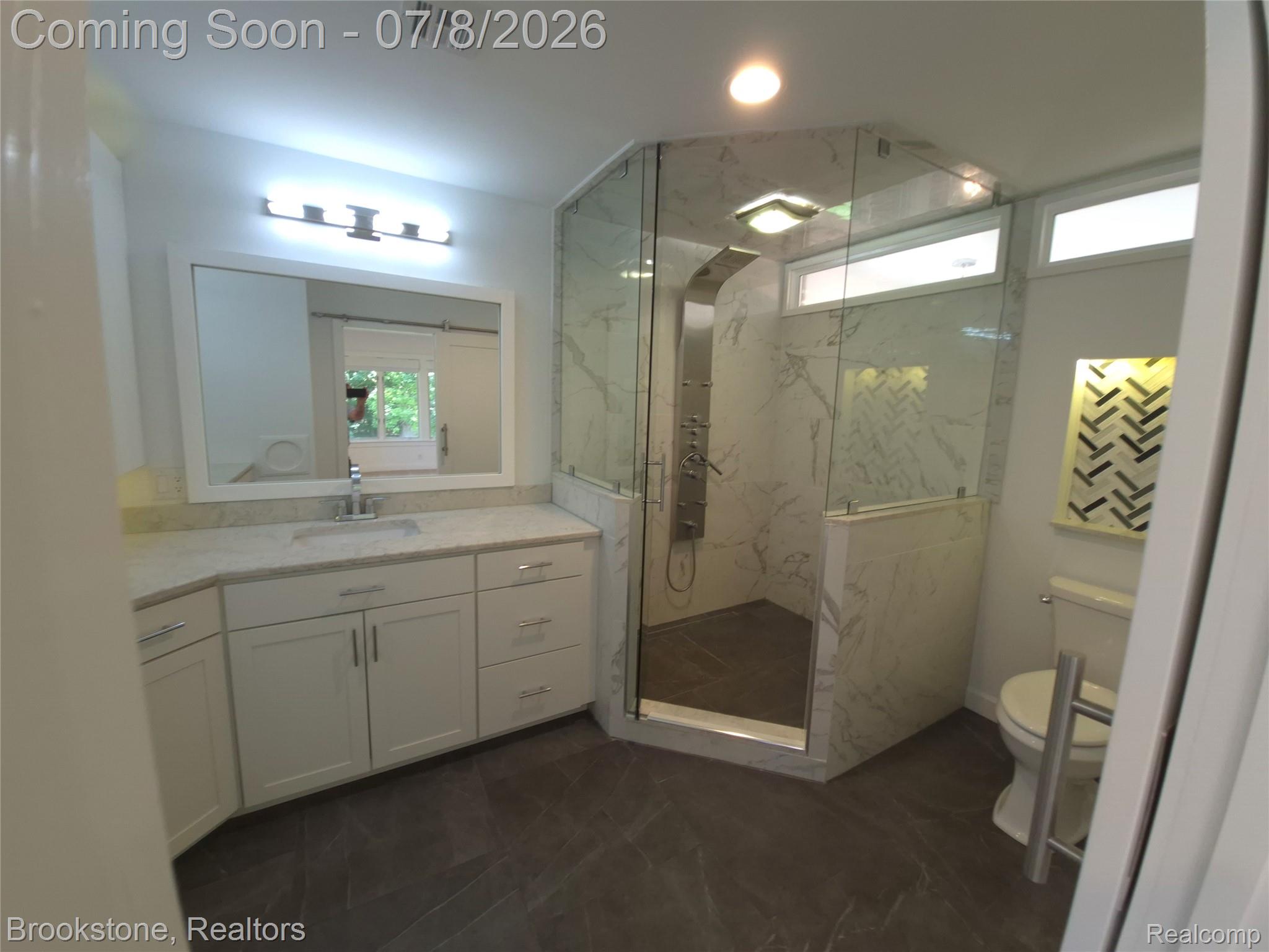 4140 South Henderson Road Davison, MI 48423 - Photo 48 of 98 Contemporary bathroom featuring a spacious glass-enclosed shower with a multi-function shower panel, white vanity with ample storage, an integrated sink, and stone-finish countertops