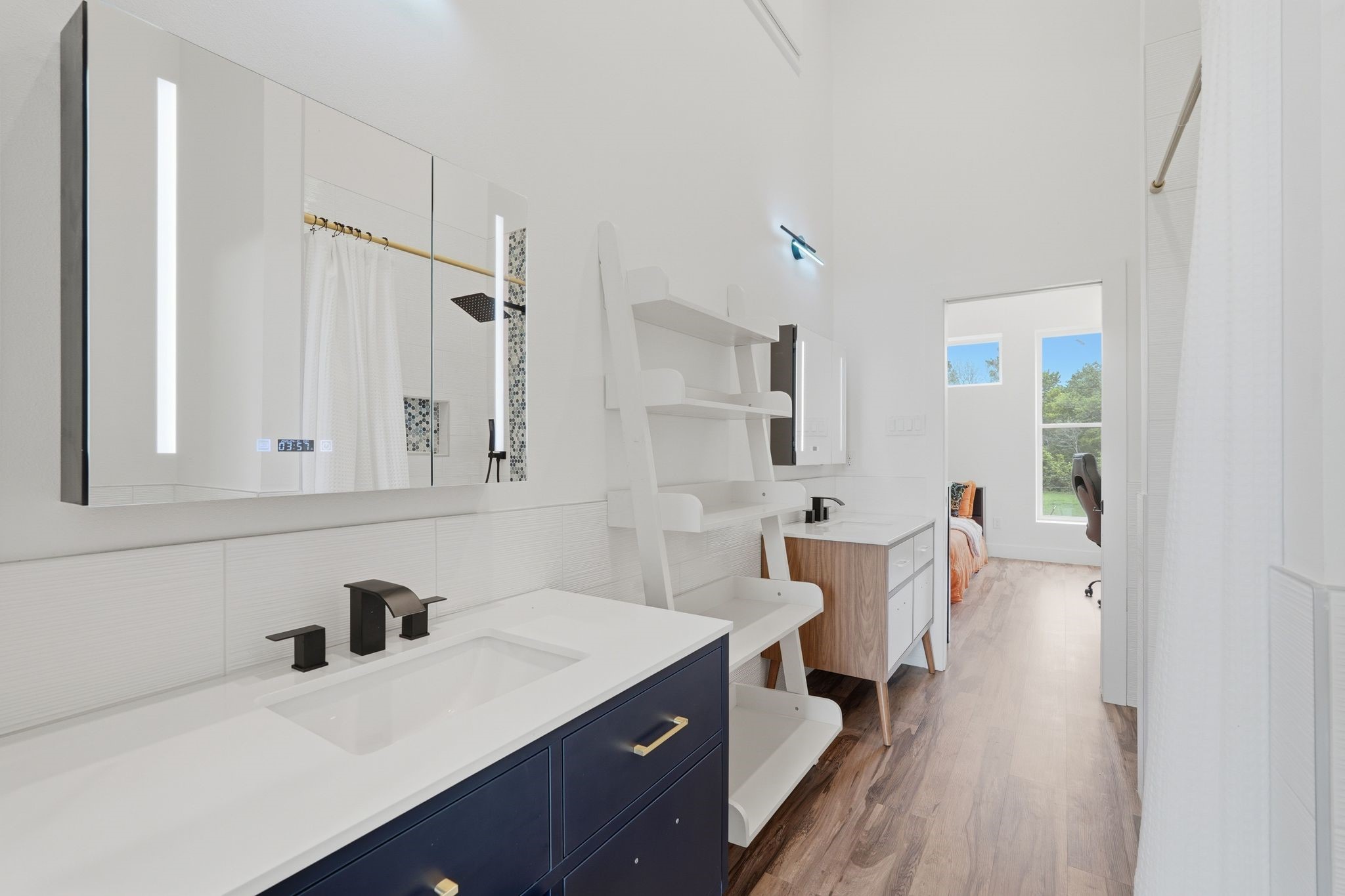 2743 Bobville Road Montgomery, TX 77316 - Photo 40 of 50 This photo showcases a modern, bright bathroom with a sleek double vanity, contemporary fixtures, and ample storage. The space features a large mirror with built-in lighting and transitions into a bedroom with natural light from large windows.