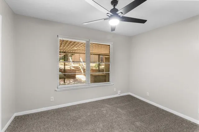 an empty room with chandelier fan and windows