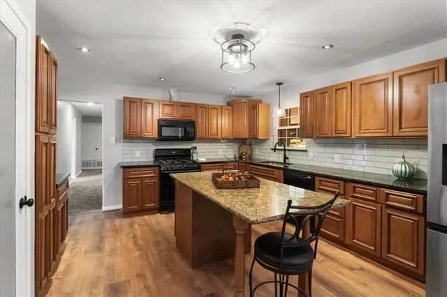 a kitchen with stainless steel appliances granite countertop a stove top oven a sink dishwasher a dining table and chairs with wooden floor