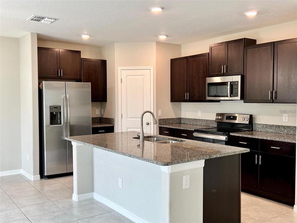 31730 Barrel Wave Way Wesley Chapel, FL 33545 - Photo 2 of 14 a kitchen with kitchen island granite countertop stainless steel appliances and wooden cabinets
