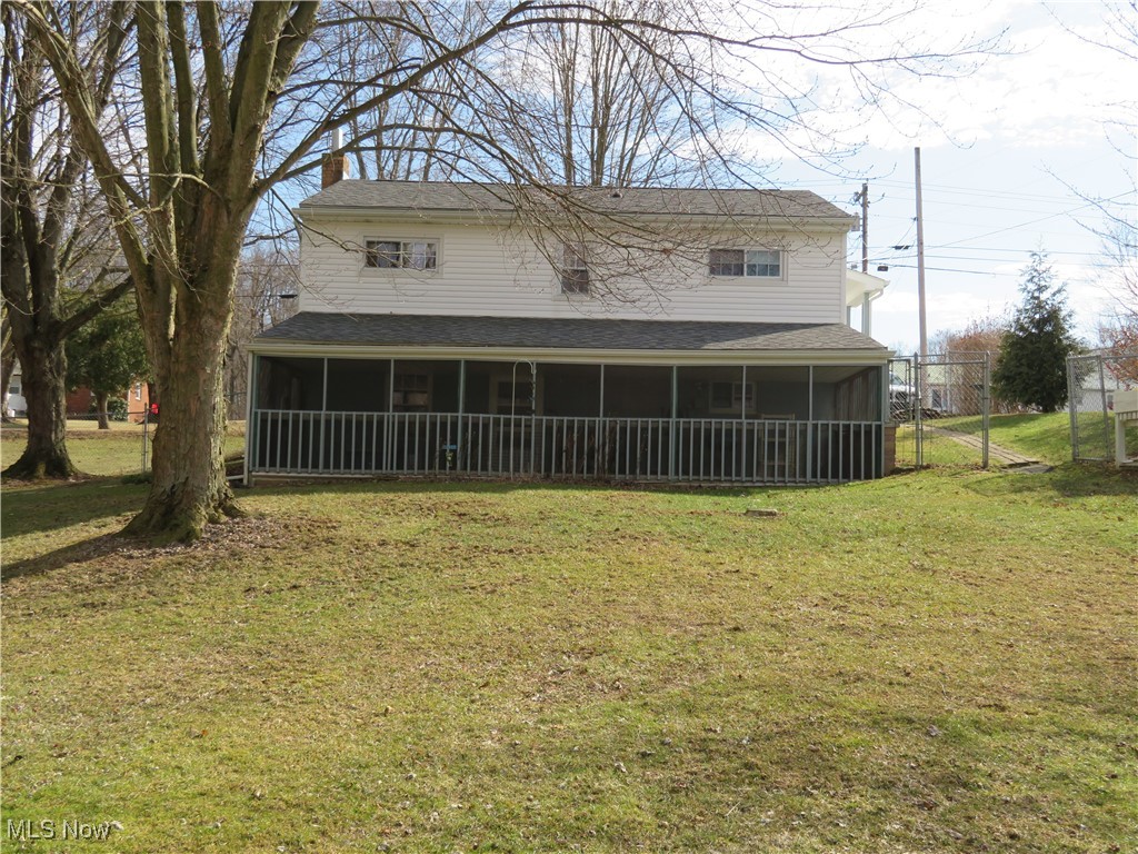 Back of house with a sunroom, a chimney, a gate, fence, and a yard