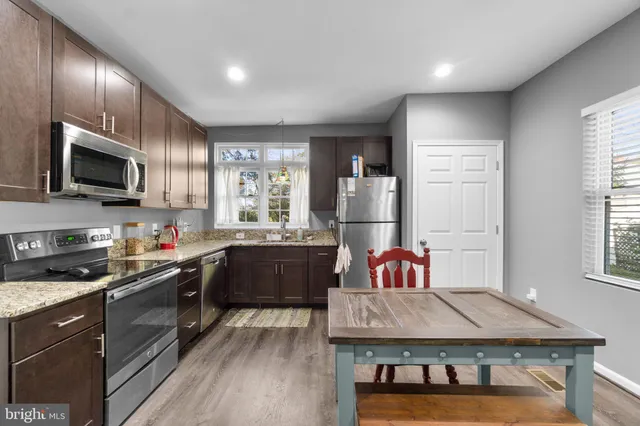 a kitchen with kitchen island granite countertop a stove top oven a sink dishwasher a dining table and chairs with wooden floor