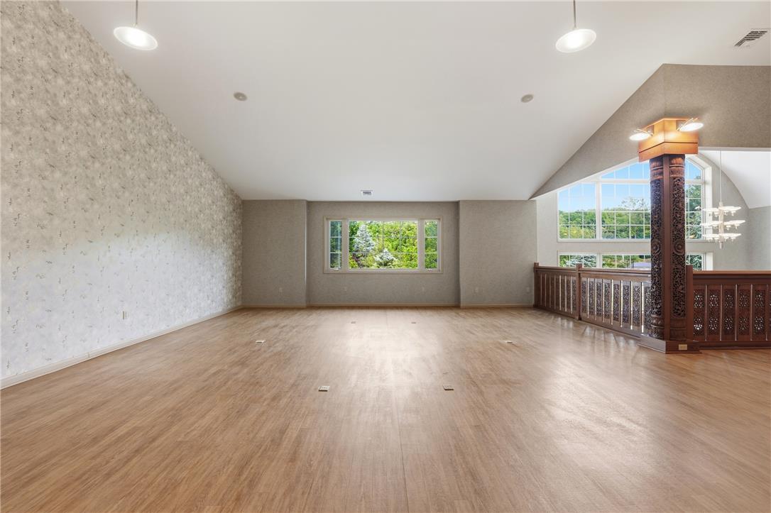 6271 Batman Road Zionsville, PA 18092 - Photo 73 of 100 A spacious, airy room features lustrous hardwood flooring and an ornate banister leading to an elevated area, complemented by large windows that offer verdant outdoor views.
