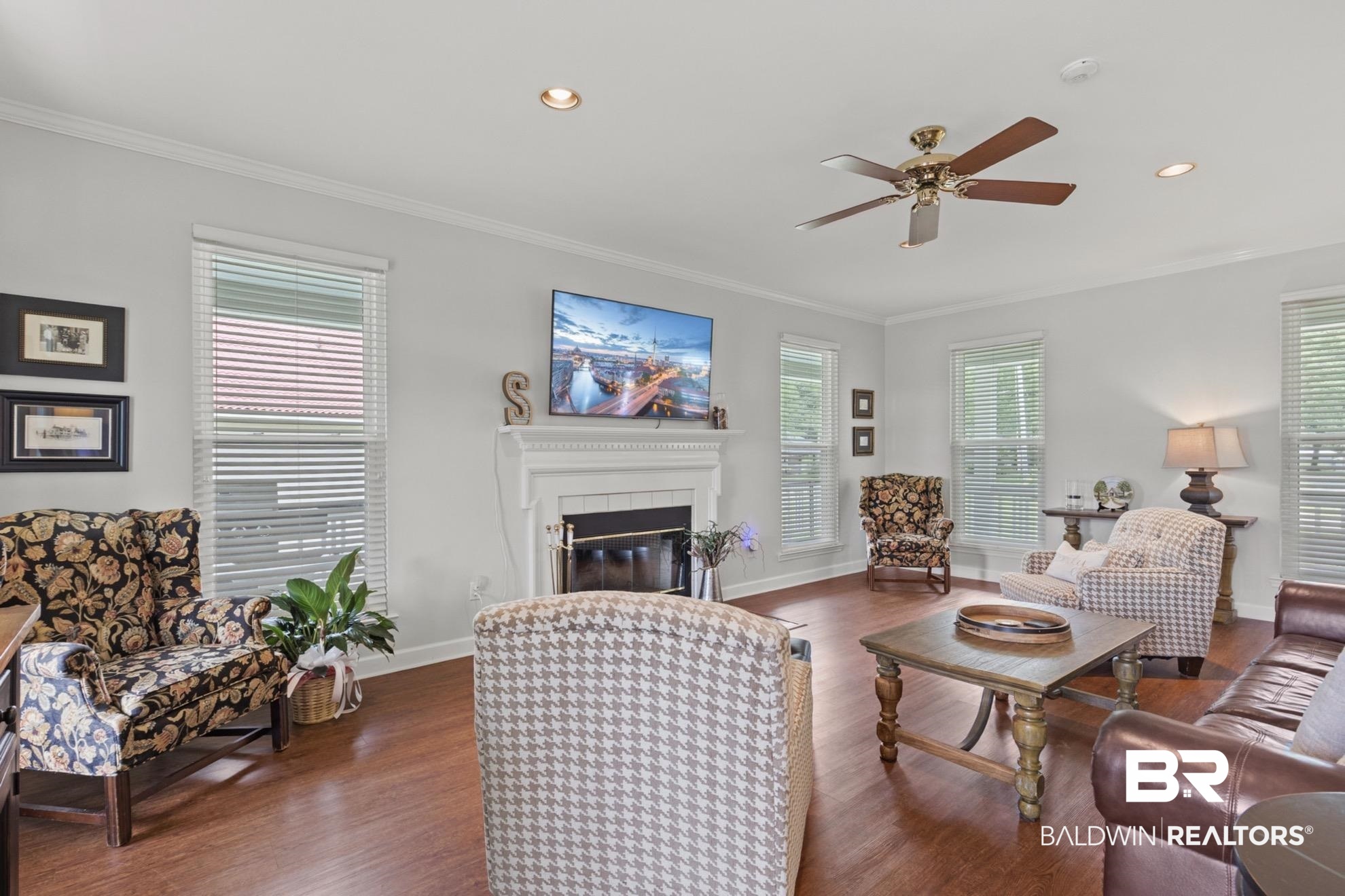 12171 Marguerite Drive Coden, AL 36523 - Photo 6 of 44 Spacious living area featuring wood-finish flooring, a fireplace with a white mantel, and multiple windows with blinds