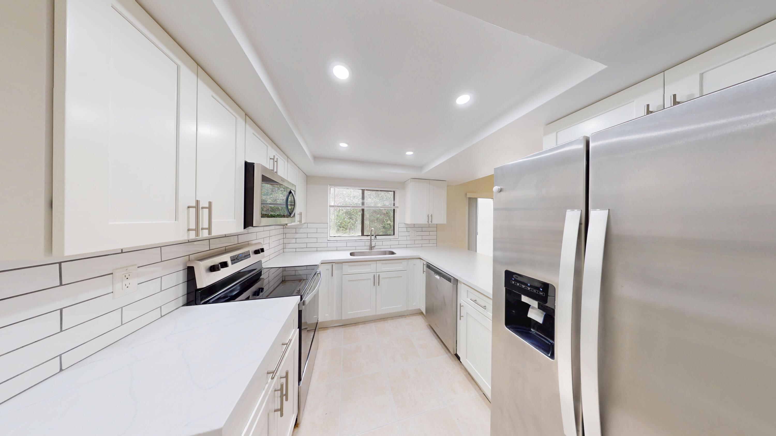 3143 Kingswood Terrace Boca Raton, FL 33431 - Photo 11 of 21 a large white kitchen with stainless steel appliances granite countertop a refrigerator a sink dishwasher a stove and white cabinets with wooden floor