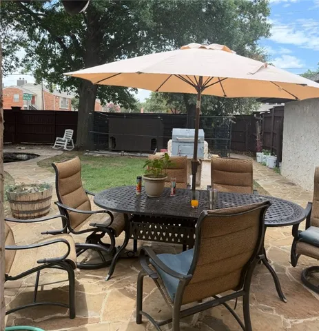 a view of a patio with a dining table and chairs under an umbrella with a barbeque