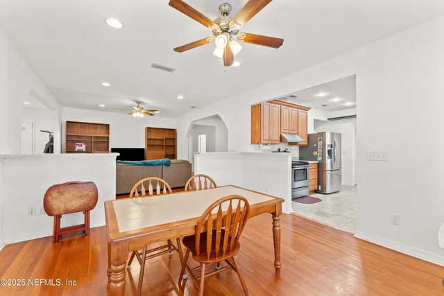 a kitchen with stainless steel appliances kitchen island granite countertop a dining table chairs and a refrigerator