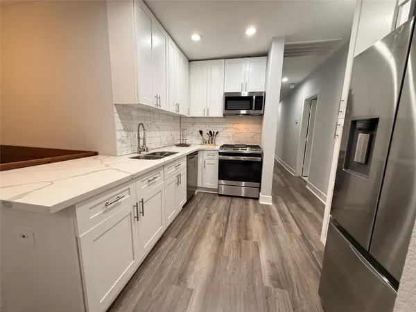 a large white kitchen with stainless steel appliances granite countertop a stove a sink and a refrigerator