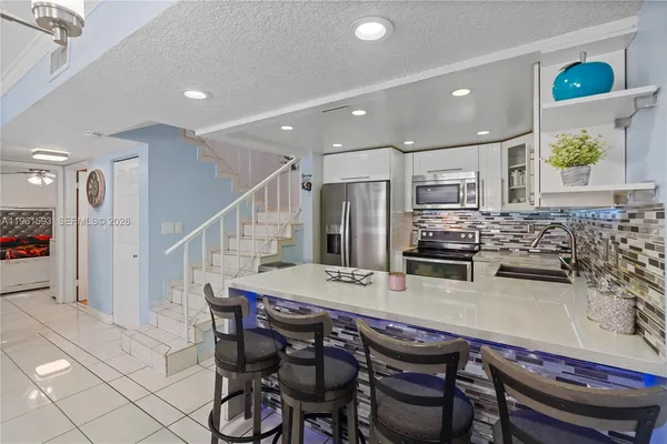 a kitchen with stainless steel appliances kitchen island granite countertop a dining table chairs and a refrigerator