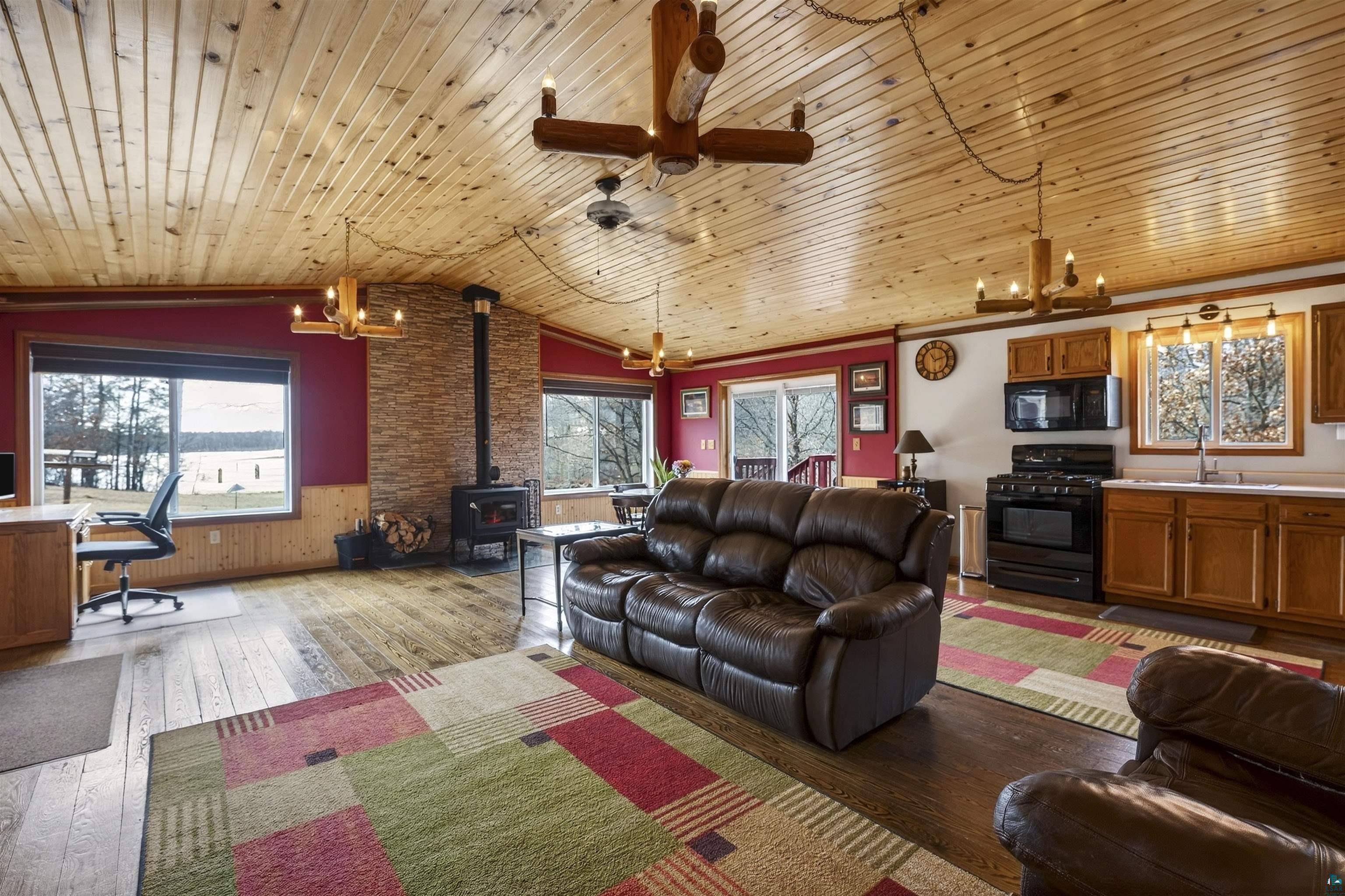 11702 East Mail Road Gordon, WI 54838 - Photo 23 of 43 Living room with hanging lights, a wood stove, light wood-style flooring, a desk, and a ceiling fan