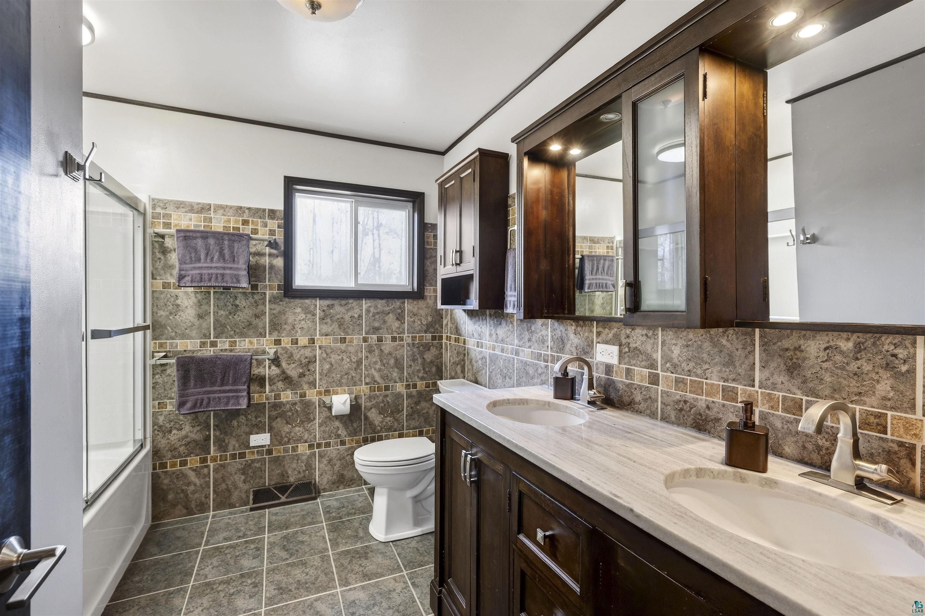 11702 East Mail Road Gordon, WI 54838 - Photo 36 of 43 Full bath featuring double vanity, enclosed tub / shower combo, dark tile patterned floors, crown molding, and tile walls