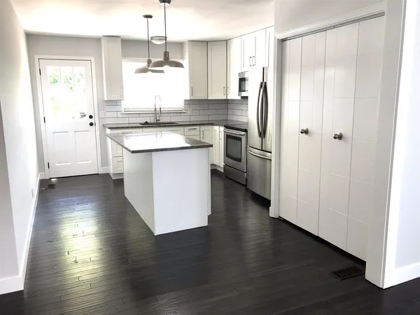 a kitchen with stainless steel appliances granite countertop a refrigerator a sink dishwasher a stove and white countertops with wooden floor