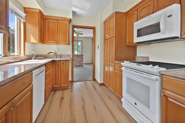 a kitchen with stainless steel appliances granite countertop a refrigerator a sink dishwasher a stove and white countertops with wooden floor