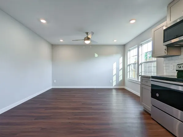 an empty room with wooden floor a ceiling fan and windows