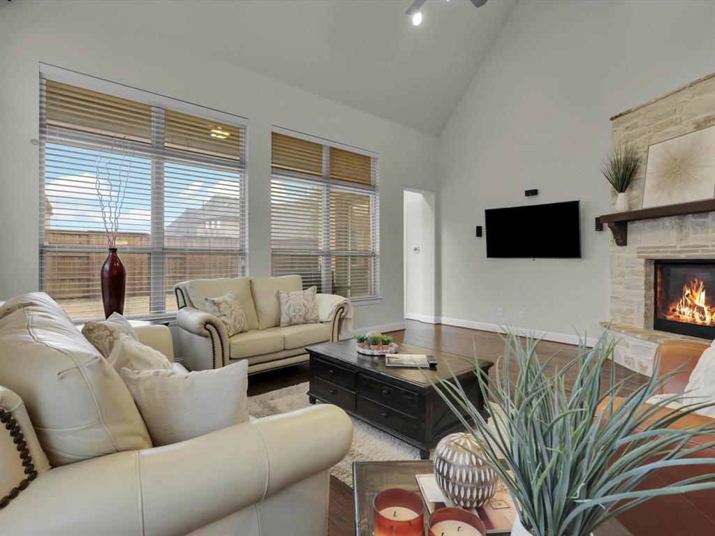 Living room featuring a stone fireplace, hardwood floors, and high vaulted ceiling.