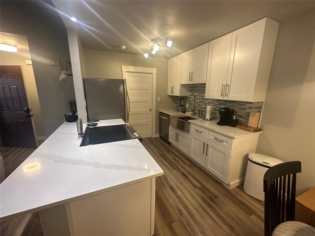3059 Hells Gate Loop, Unit 8 Strawn, TX 76475 - Photo 16 of 26 a kitchen with stainless steel appliances a stove a refrigerator a sink and white cabinets with wooden floor