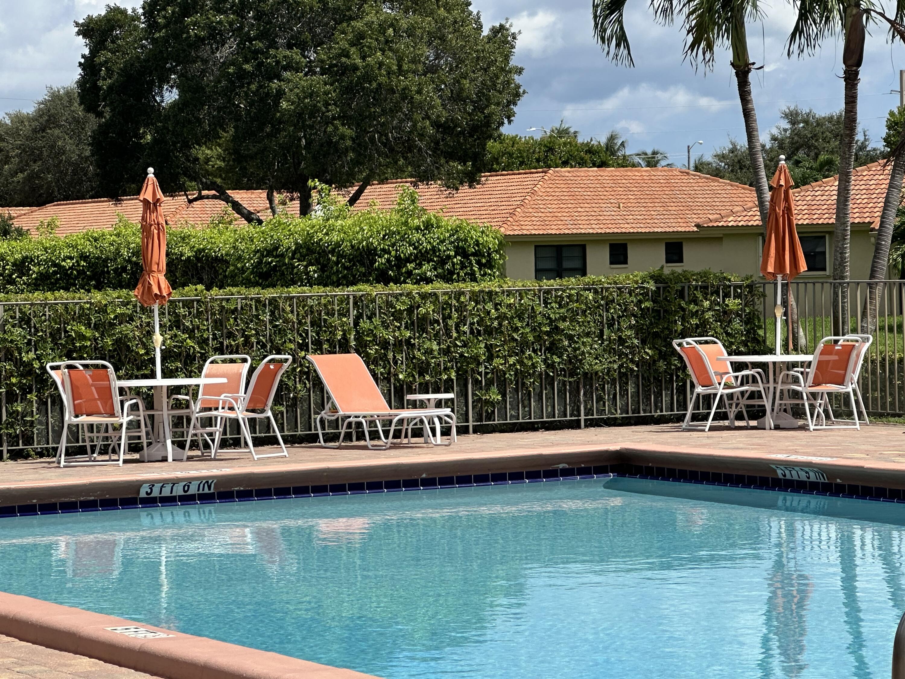 9845 Pineapple Tree Drive, Unit 208 Boynton Beach, FL 33436 - Photo 15 of 21 a view of a lake with couches chairs under an umbrella